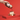 A hand sprinkles cocoa powder from a decorative tin onto a round dessert topped with cream, set on a gold stand against a vibrant red background.