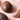 Assorted chocolate eggs in various shades of brown and cream are arranged on a light pink background. The eggs have smooth and faceted surfaces with geometric patterns.