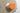 An orange heart-shaped box and a floral-patterned Best wishes card rest on a beige tablecloth, with part of a glass dish visible at the top left corner. - AI generated text